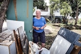 A 75-year-old woman standing in the front yard of a home behind a pile of debris from the flood.