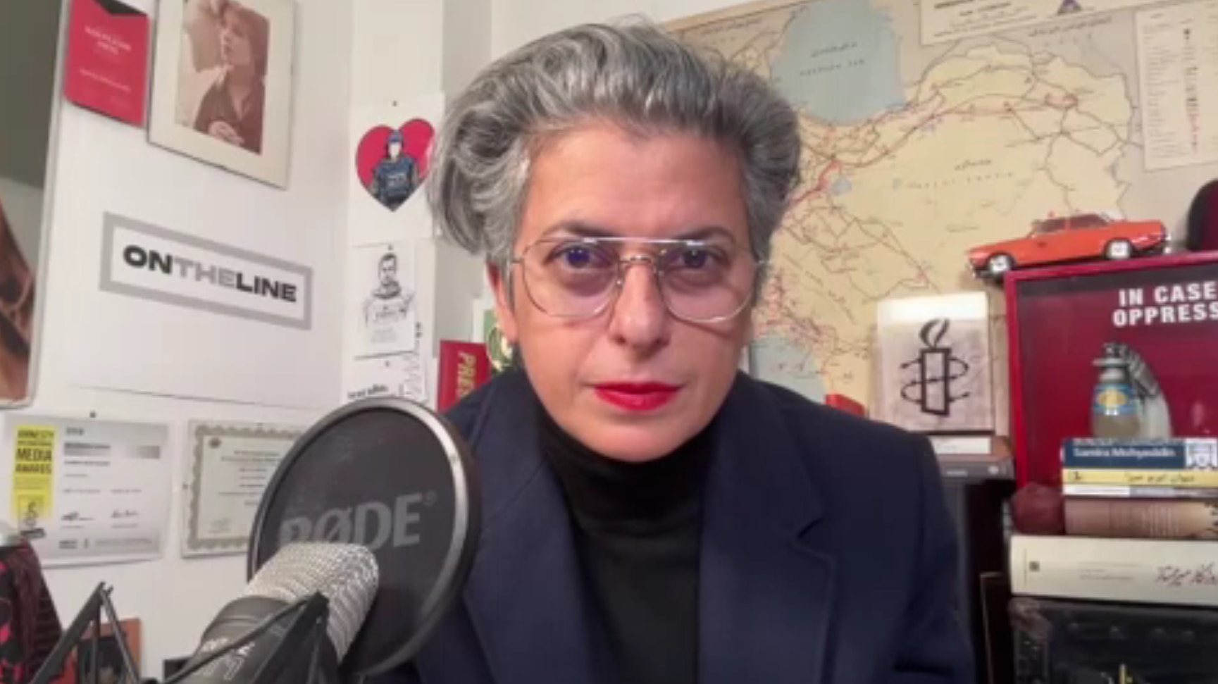 Uma mulher de óculos está sentada em frente a um microfone.