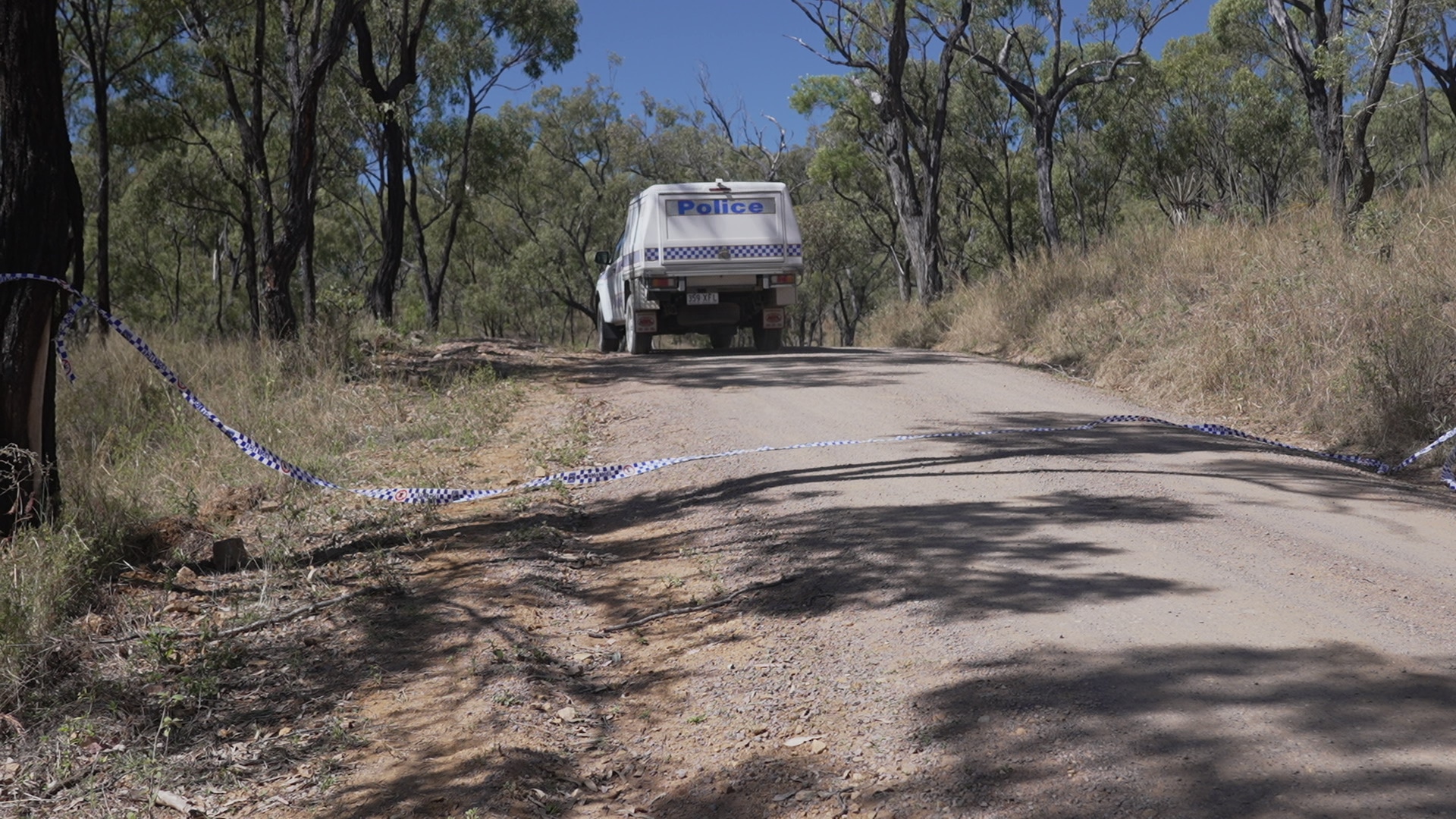A police vehicle sits in the middle of a country road with police tape in the foreground