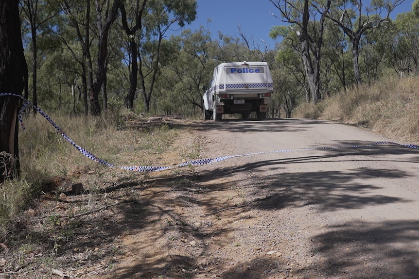 A police vehicle sits in the middle of a country road with police tape in the foreground