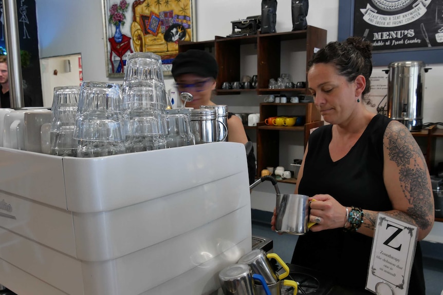 A woman makes a cup of coffee standing behind  counter in a cafe.