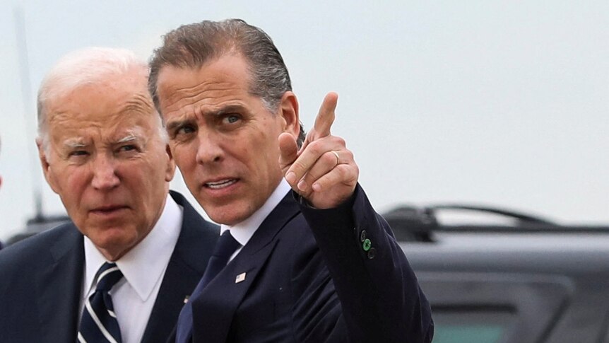 Joe Biden stands behind Hunter Biden, who is pointing at something. A black car is in the background.