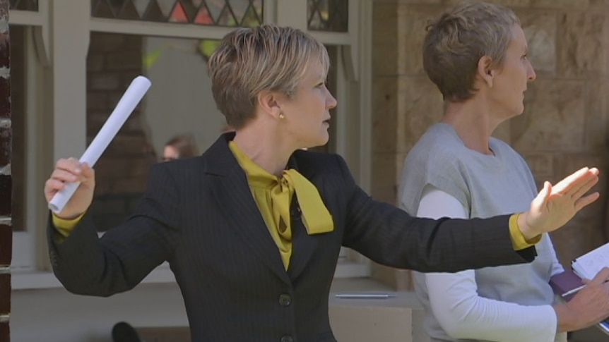 Female auctioneer stands in front of house with arms spread wide