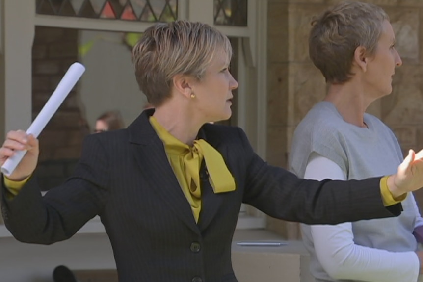 Female auctioneer stands in front of house with arms spread wide