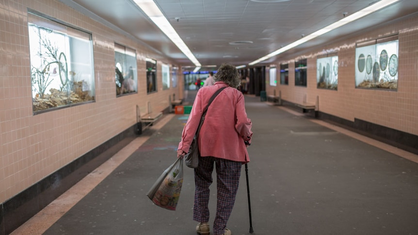 An older woman walks through an underground Melbourne train station.