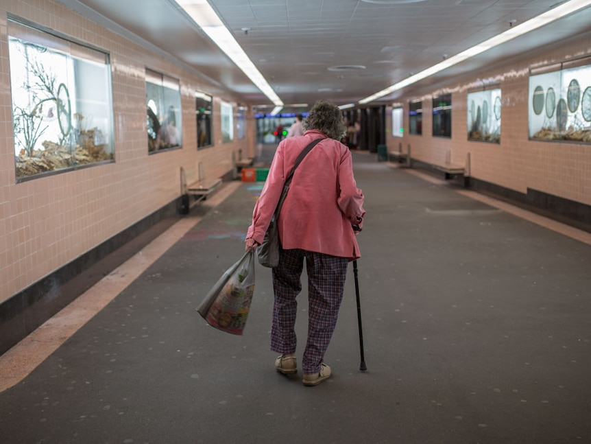 An older woman walks through an underground Melbourne train station.