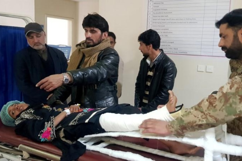 Samina Bibi lying on a hospital bed surrounded by people.