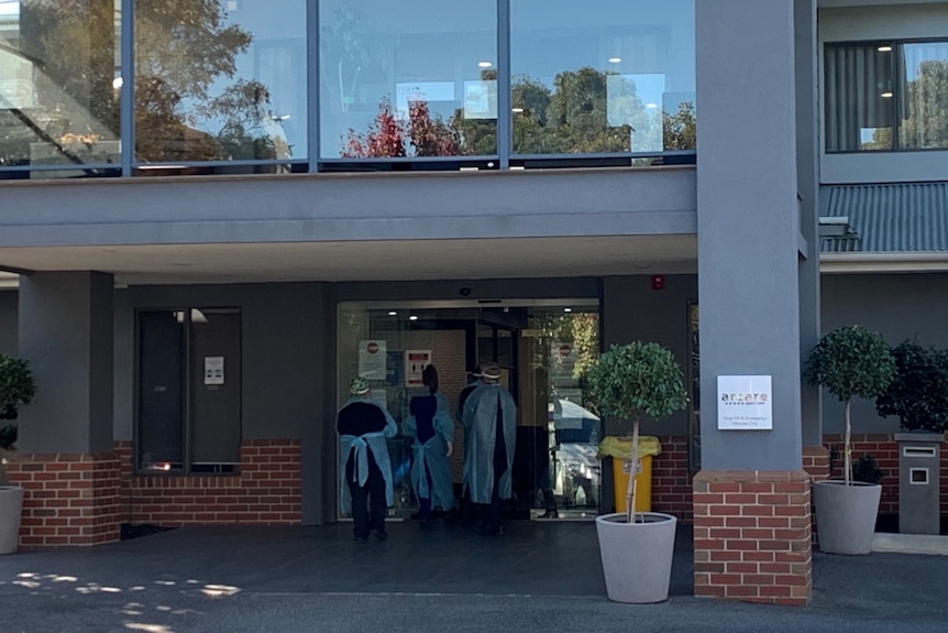 People wearing protective clothing enter front doors of a brick building.