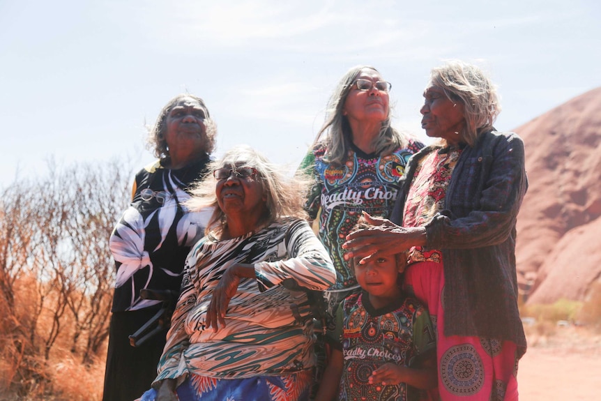 A group of traditional owners stand at the base of Uluru.