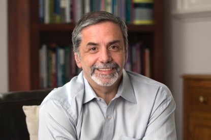 a man sits in front of a bookcase smiling