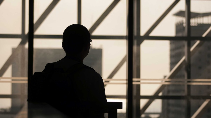 Silhouette of person in empty office building looking out a window.