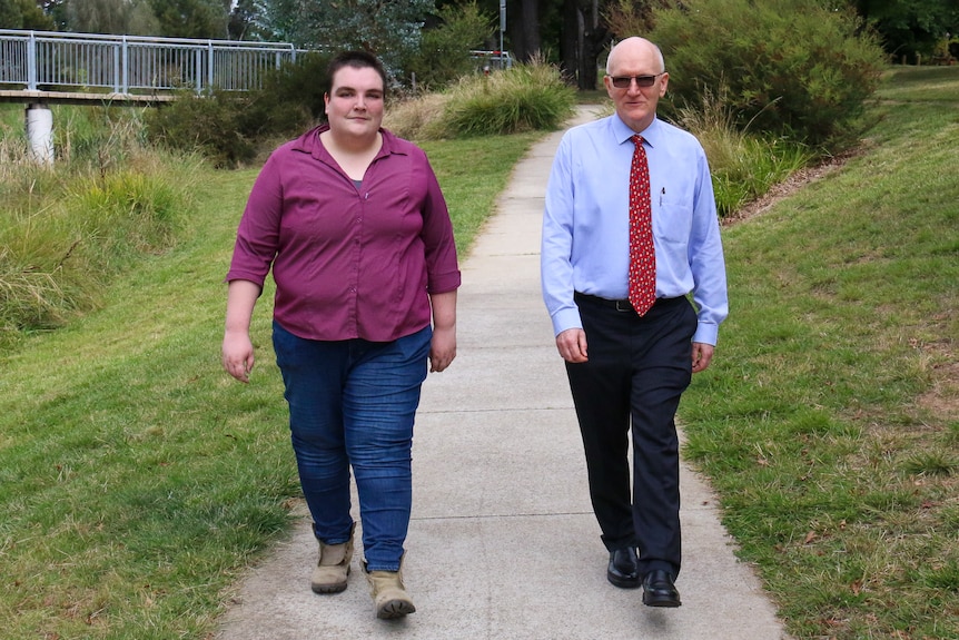 Two people walking together, one wearing a magenta shirt and the other wearing a collared shirt tie. 
