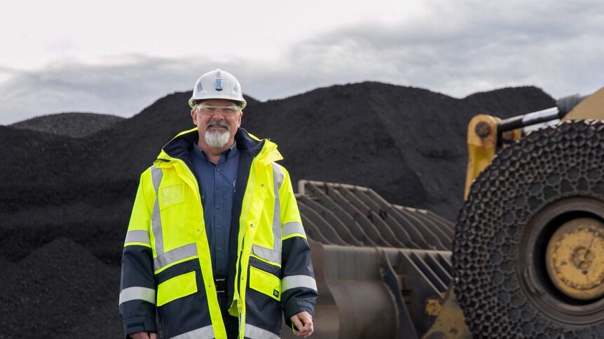 A man in high visibility gear in front of a pile of coal and heavy machinery