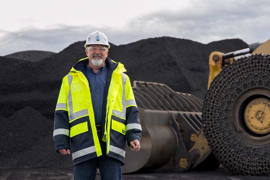 A man in high visibility gear in front of a pile of coal and heavy machinery