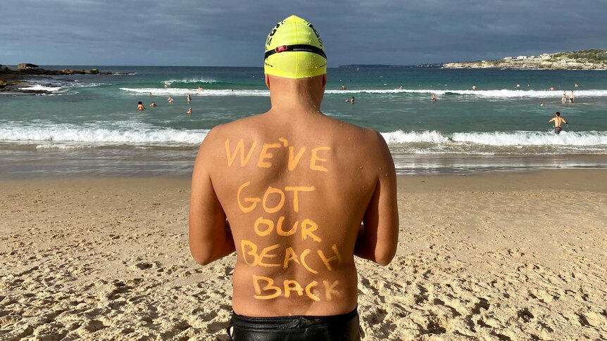 A swimmer facing the beach, with 'We've got our beach back' written in zinc on his back.