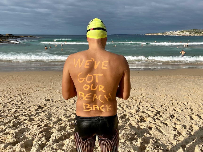 A swimmer facing the beach, with 'We've got our beach back' written in zinc on his back.