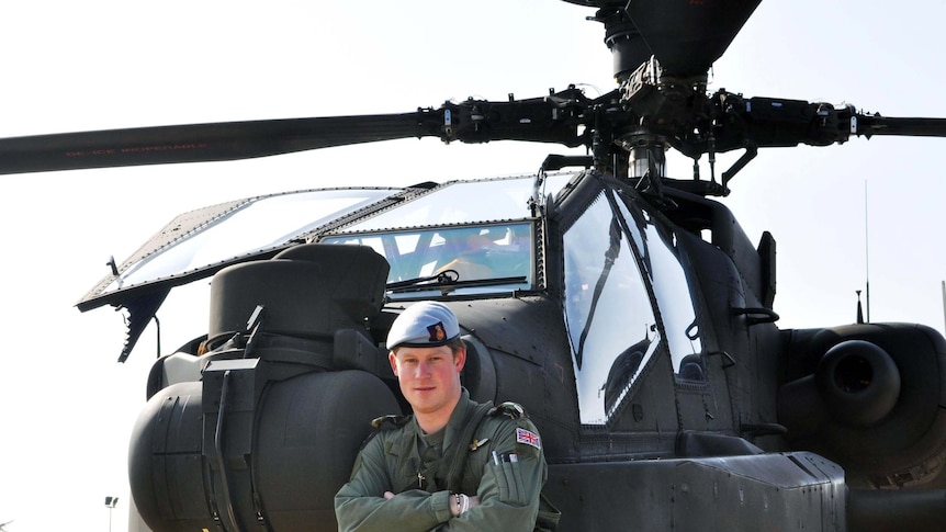 Prince Harry stands in front of an Apache Helicopter