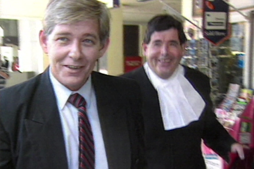 Two men smile as they walk near each other. One man is in barrister's robes.