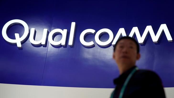 Qualcomm sign on blue background with Chinese man standing in front