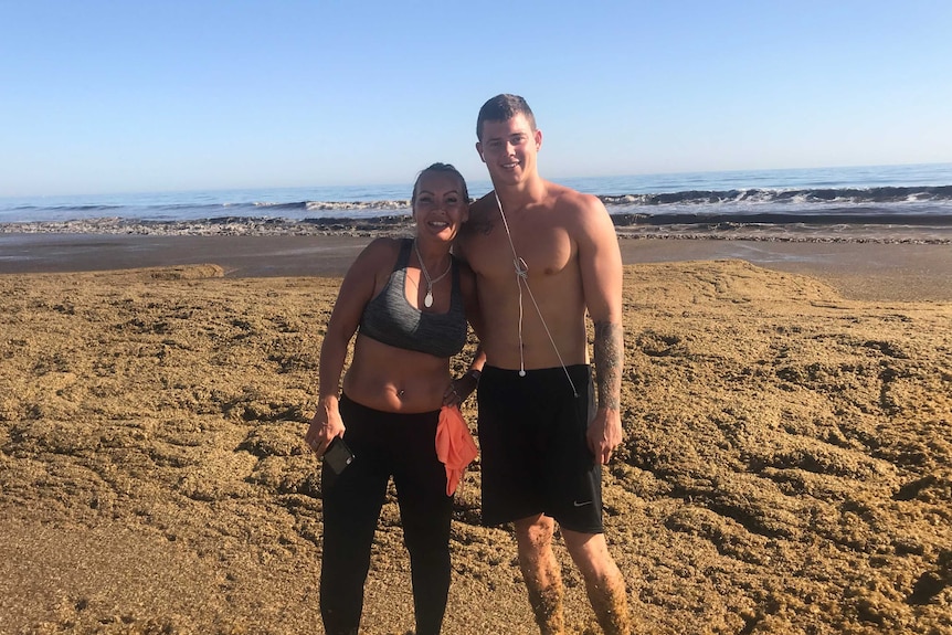 Couple stand amid mass of seaweed on Gold Coast beach.