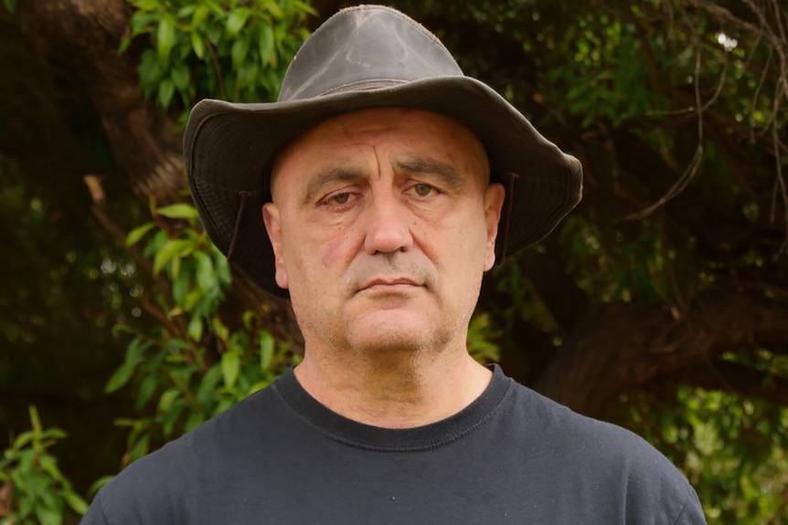 A head and shoulders shot of a man wearing a wide-brimmed hat standing posing for a photo.