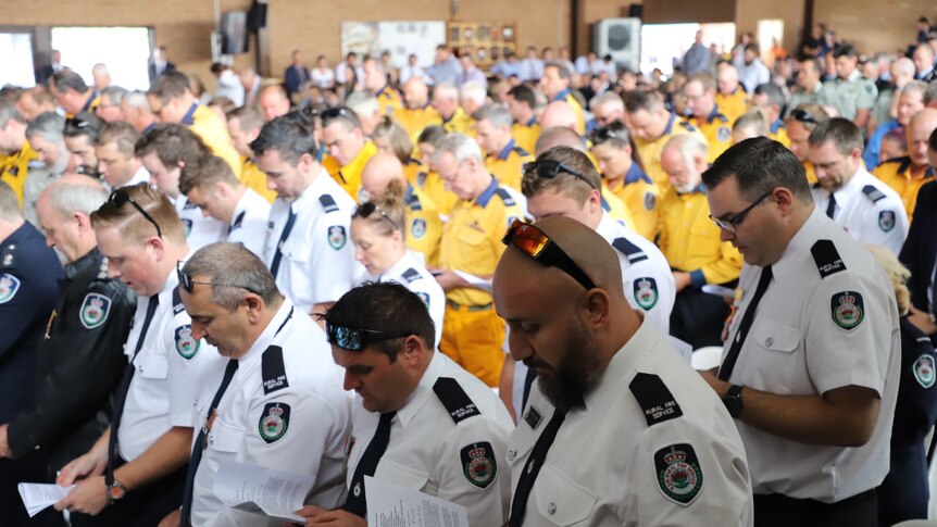 A crowd of uniformed firefighters read from their funeral booklets inside the Holbrook basketball hall.