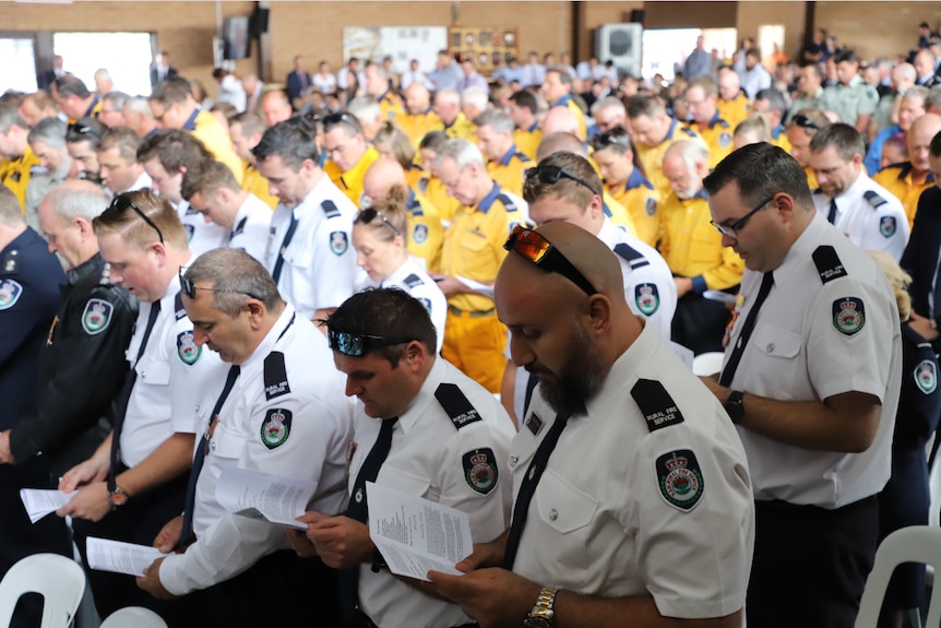A crowd of uniformed firefighters read from their funeral booklets inside the Holbrook basketball hall.
