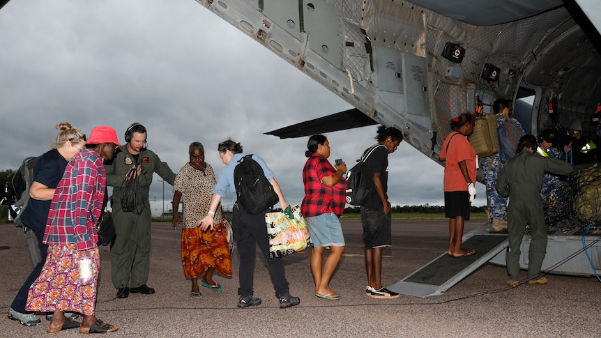 A line of people boarding an ADF aircraft on an airstrip in a remote community.