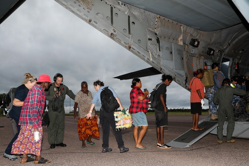 A line of people boarding an ADF aircraft on an airstrip in a remote community.