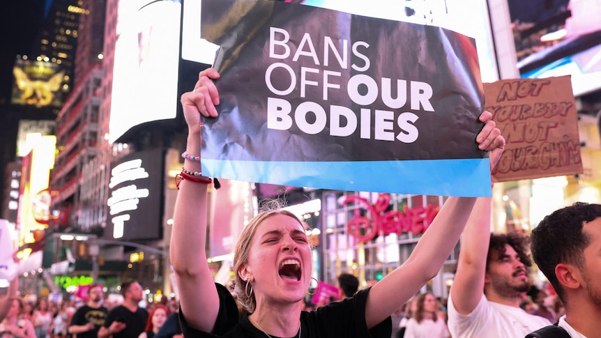 A woman marches down a street holding a sign that says "bans off our bodies"