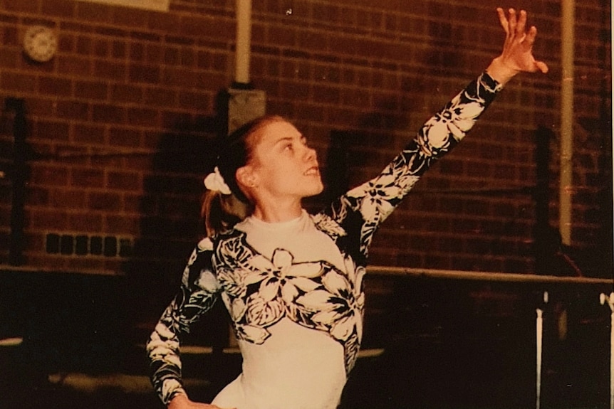 A girl in a leotard poses with her hand in the air.