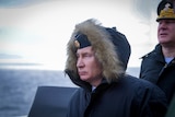 Vladimir Putin looking downcast while wearing a fur trimmed hooded coat at sea