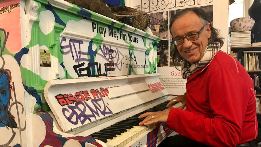 Paulie Steward sits at a piano which is decorated with graffiti reading: Play me, I'm yours