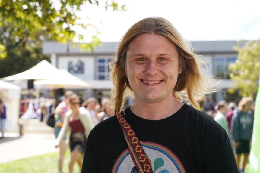 A smiling person with long, fair hair standing at an outdoor event.
