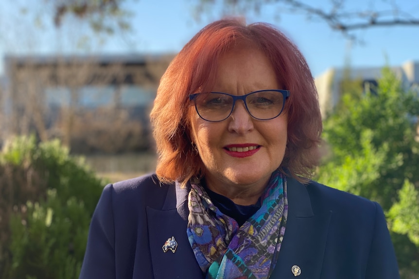 Doctor Karen Price, a woman with mid-lenth red hair, smiles at the camera outdoors.