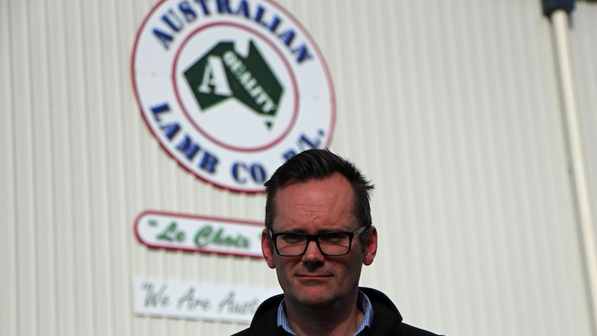 A man with glasses standing outside a shed