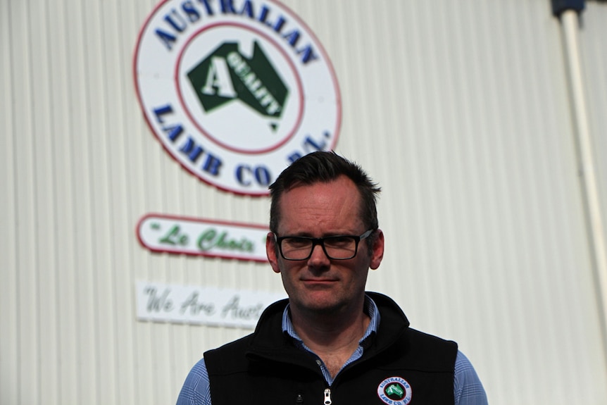 A man with glasses standing outside a shed