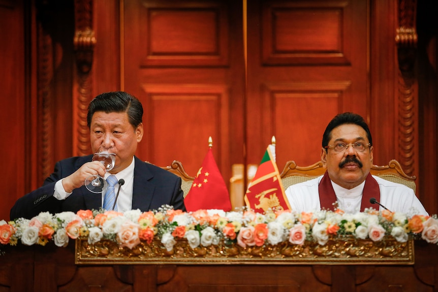 Xi Jinping sips a glass of water while seated next to Mahinda Rajapaksa