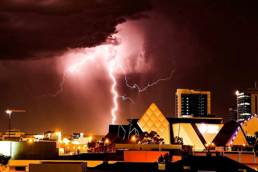 A bright bolt of lightning emerging from a dark purple sky over buildings in Perth's CBD.