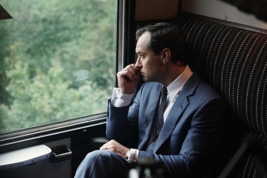 Jude Law in a suit on a train staring out the window stressed in the film The Nest