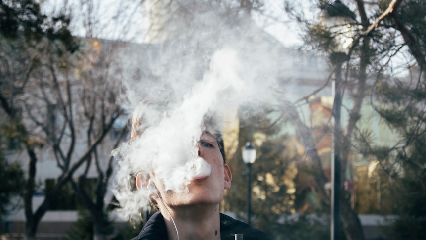 A close-up of a teenage boy exhaling vapour from an e-cigarette.