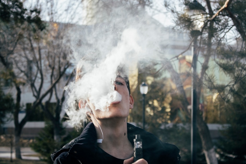 A close-up of a teenage boy exhaling vapour from an e-cigarette.