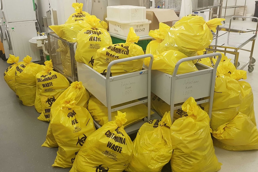 Yellow bags saying 'contaminated' lie on the ground of a lab.