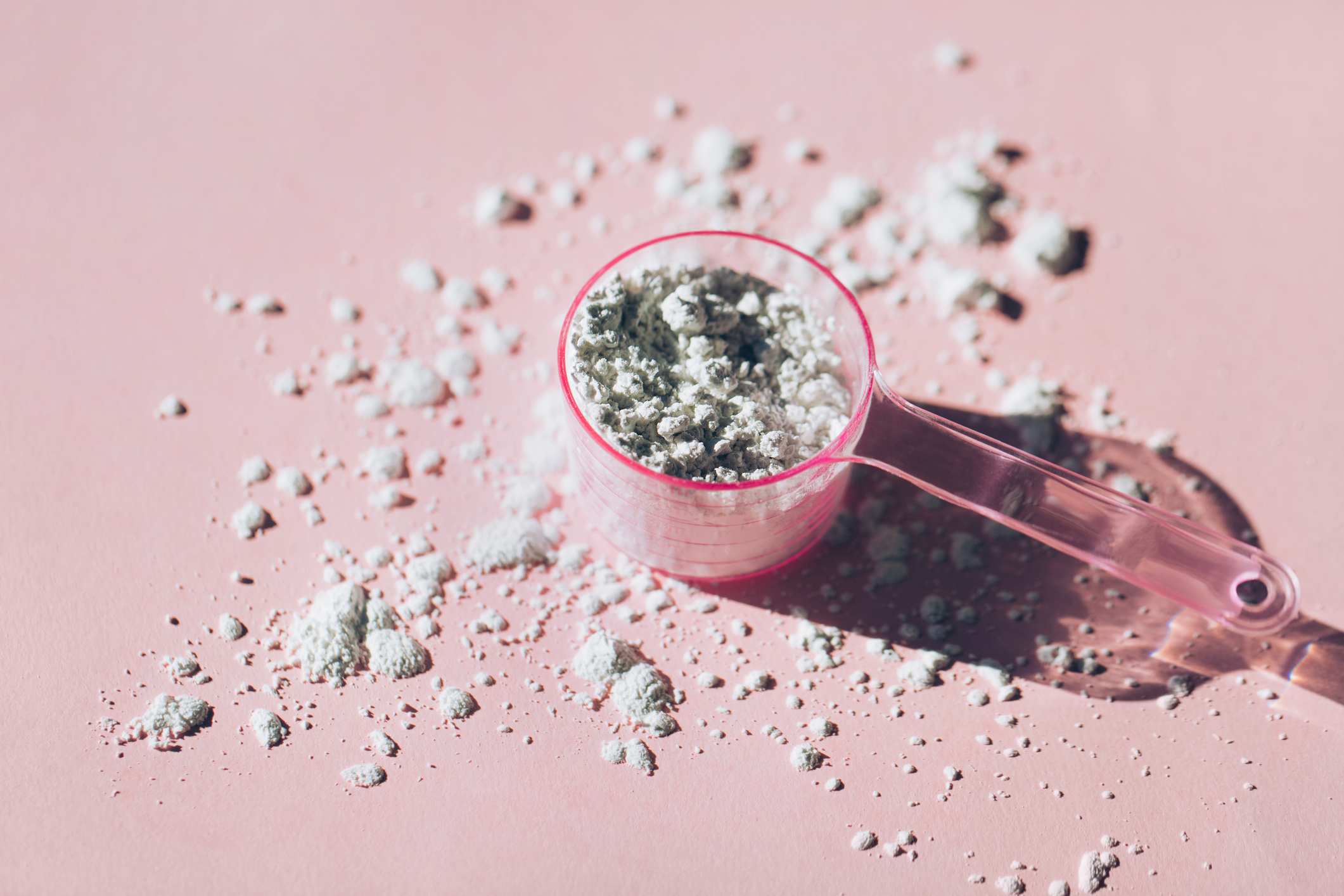 Measuring spoon filled with collagen powder with a pink background