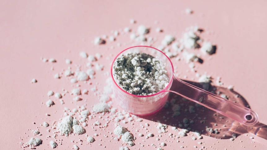 Measuring spoon filled with collagen powder with a pink background