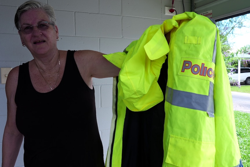 A woman in a black singlet holds up a police rain jacket