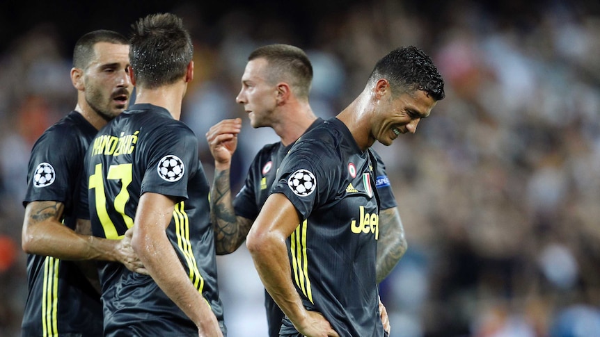 A player stands with his hands on his hips in tears, with three of his teammates in discussion behind him.