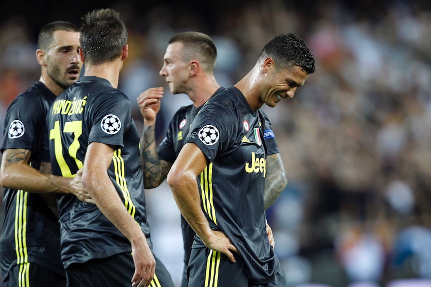 A player stands with his hands on his hips in tears, with three of his teammates in discussion behind him.