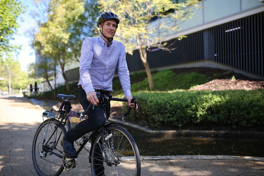 Giles wears work attire while riding a bike.