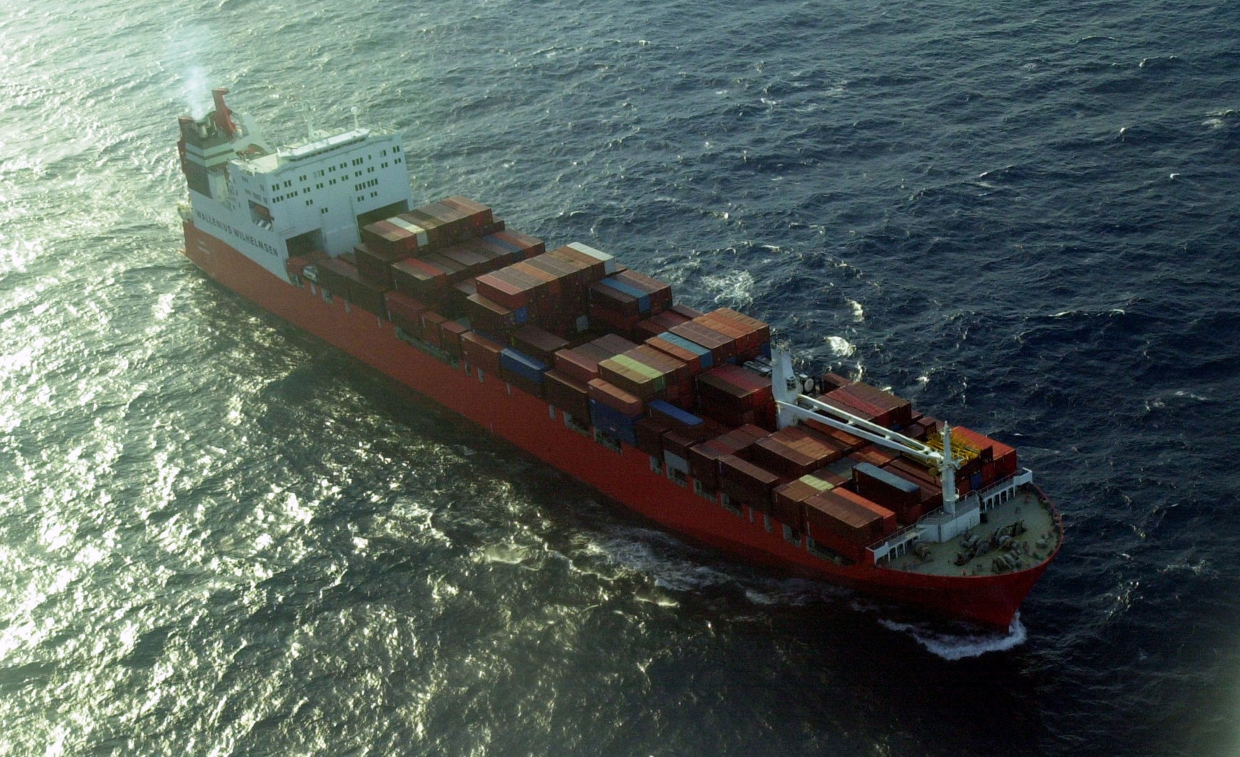 A large red freight ship at sea, with red shipping containers loaded on board.